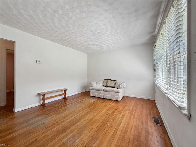 unfurnished room with baseboards, light wood-type flooring, a textured ceiling, and visible vents
