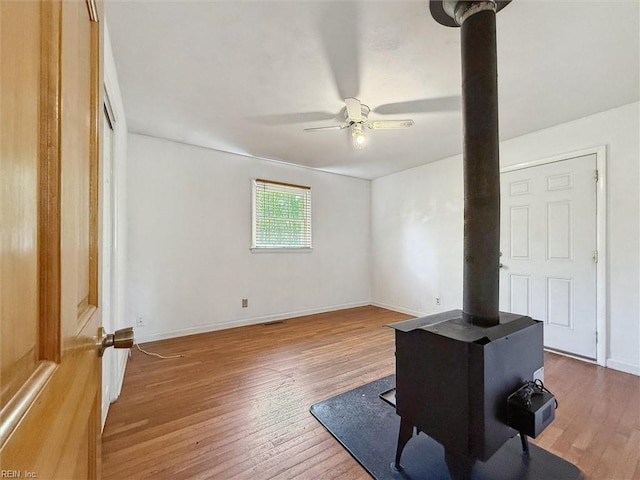 interior space with baseboards, a ceiling fan, a wood stove, and hardwood / wood-style floors