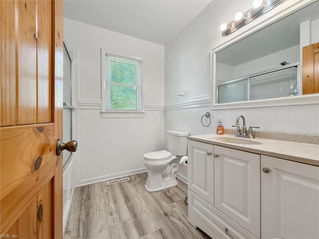 bathroom with visible vents, vanity, a shower with door, wood finished floors, and toilet