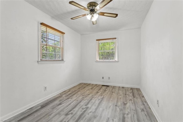 spare room featuring baseboards, a ceiling fan, light wood finished floors, and a textured ceiling