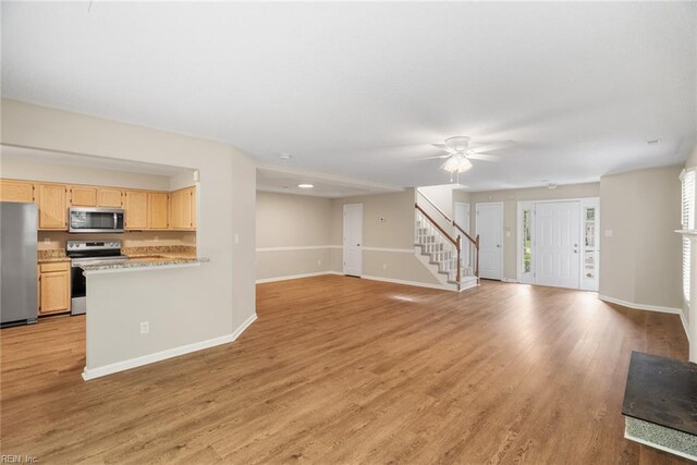 unfurnished living room with baseboards, light wood-style floors, ceiling fan, and stairway