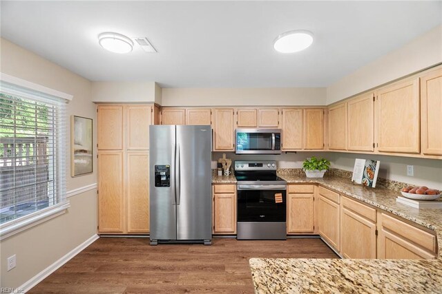 kitchen featuring light brown cabinetry, baseboards, light stone counters, stainless steel appliances, and dark wood-type flooring