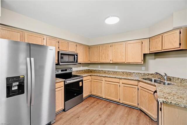 kitchen with light brown cabinets, light stone countertops, light wood-type flooring, a sink, and appliances with stainless steel finishes