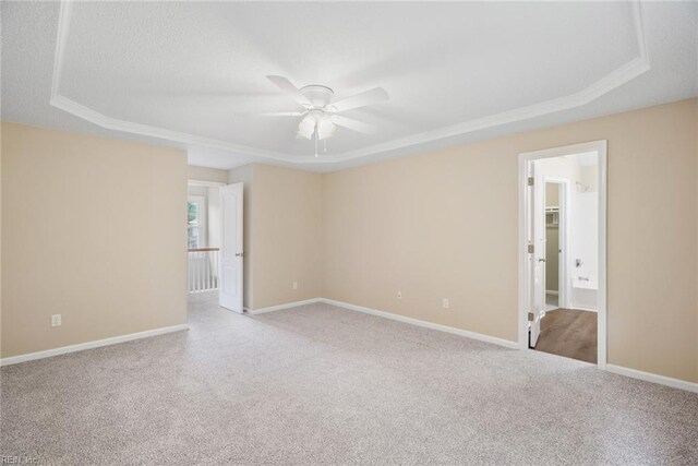 empty room featuring carpet floors, a ceiling fan, a tray ceiling, and baseboards