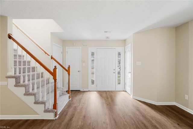 foyer entrance featuring baseboards, stairs, wood finished floors, and visible vents