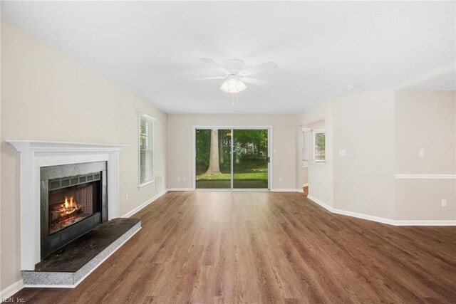 unfurnished living room with baseboards, ceiling fan, a lit fireplace, and wood finished floors