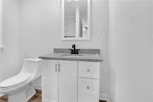 half bathroom with vanity, baseboards, toilet, and wood finished floors