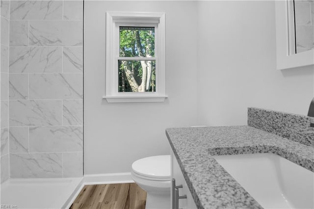bathroom featuring vanity, toilet, baseboards, wood finished floors, and tiled shower