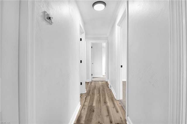 hall with light wood-type flooring, ornamental molding, and baseboards