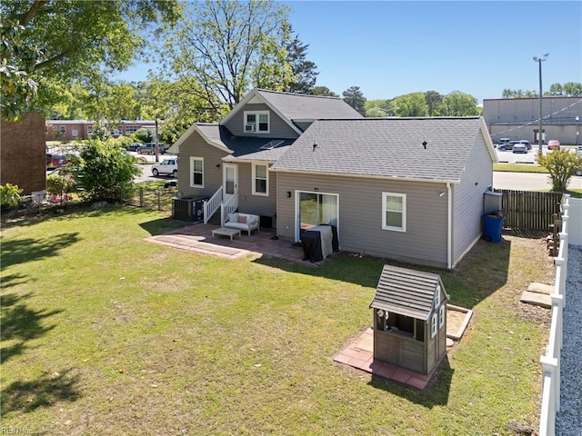 rear view of property with fence, cooling unit, roof with shingles, a patio area, and a lawn
