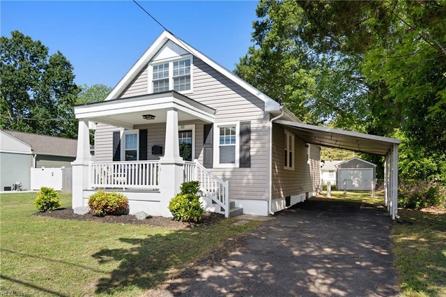 bungalow-style house with a porch, a front yard, an outdoor structure, aphalt driveway, and an attached carport