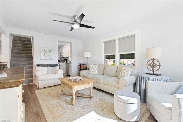 living area with light wood-type flooring, ceiling fan, and stairway
