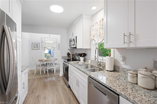kitchen with white cabinets, light stone counters, appliances with stainless steel finishes, a sink, and light wood-type flooring