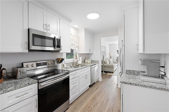 kitchen featuring appliances with stainless steel finishes, a sink, light stone counters, white cabinets, and light wood-style flooring