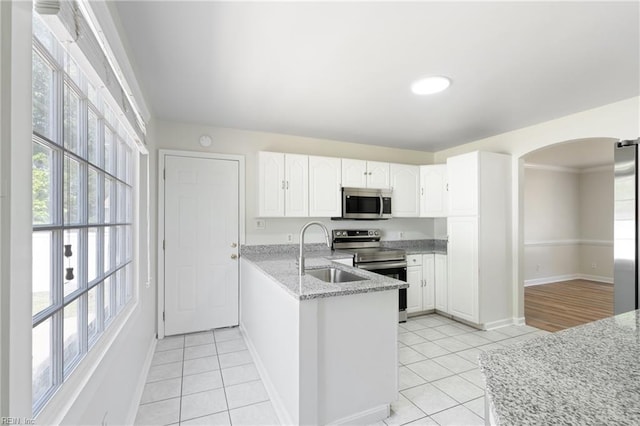 kitchen with a peninsula, arched walkways, white cabinets, a sink, and stainless steel appliances