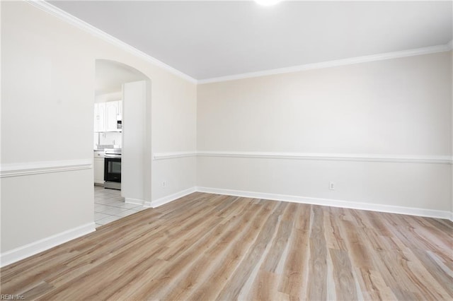 unfurnished room featuring arched walkways, baseboards, ornamental molding, and light wood-style flooring