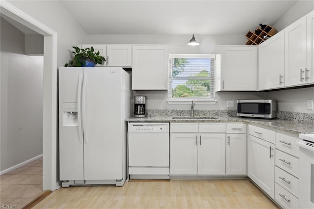 kitchen featuring white appliances, white cabinetry, light stone counters, a sink, and light wood finished floors