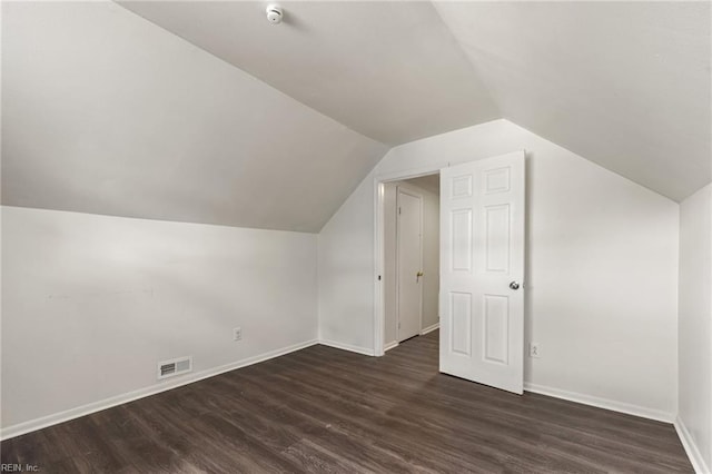 additional living space featuring baseboards, dark wood-type flooring, lofted ceiling, and visible vents