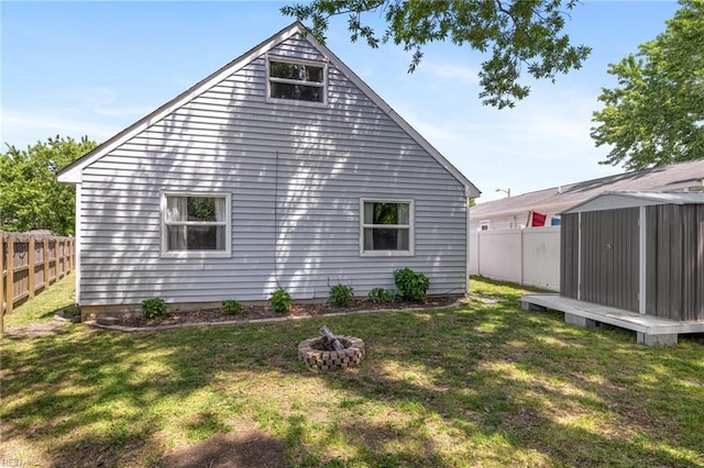 rear view of house with a storage unit, an outdoor fire pit, a fenced backyard, an outbuilding, and a lawn