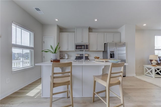 kitchen featuring appliances with stainless steel finishes, light wood-style floors, light countertops, visible vents, and a center island with sink