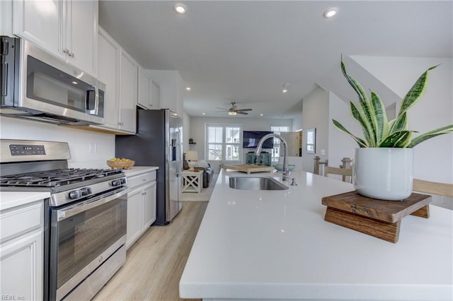 kitchen with recessed lighting, white cabinets, a sink, light wood-style flooring, and stainless steel appliances
