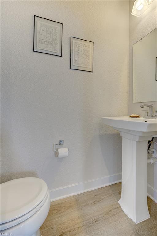 half bathroom featuring baseboards, toilet, and wood finished floors