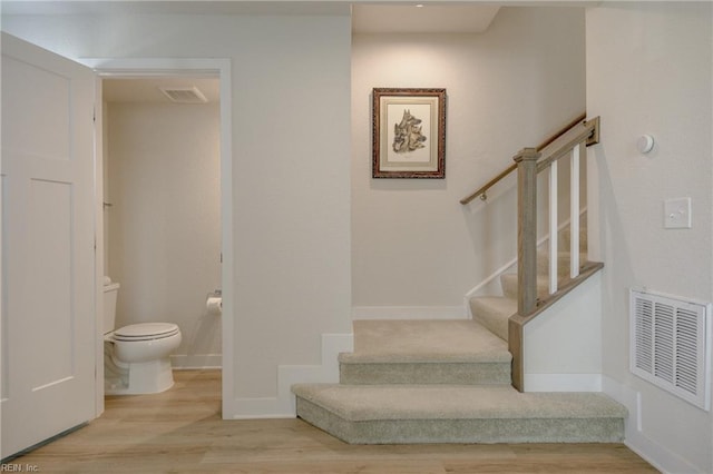 stairway with baseboards, visible vents, and wood finished floors
