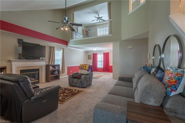 carpeted living area with a ceiling fan, high vaulted ceiling, a glass covered fireplace, and baseboards