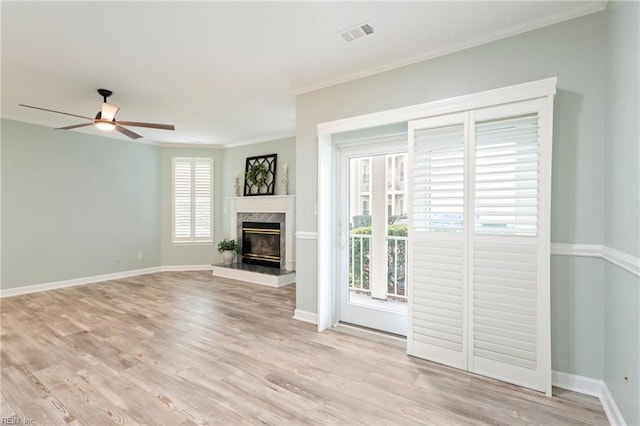 unfurnished living room with visible vents, ornamental molding, light wood-style floors, baseboards, and ceiling fan