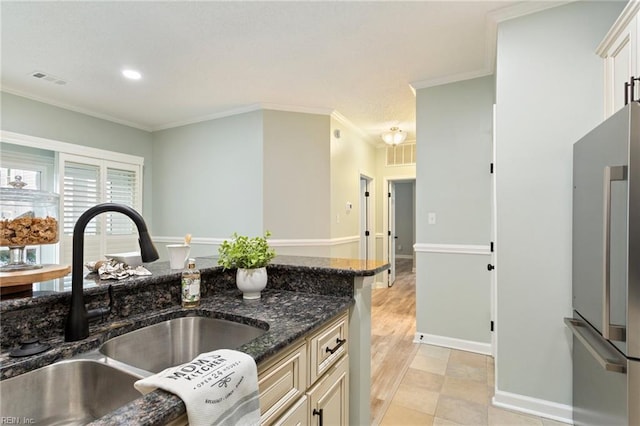 kitchen featuring crown molding, stainless steel fridge, a sink, dark stone countertops, and visible vents