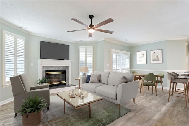 living room with ceiling fan, ornamental molding, light wood finished floors, and visible vents