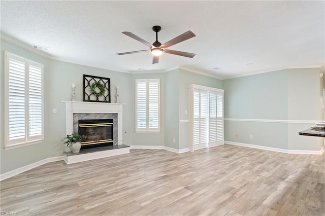 unfurnished living room featuring crown molding, a premium fireplace, a ceiling fan, light wood-type flooring, and visible vents