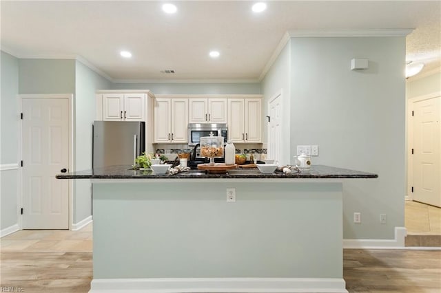 kitchen featuring crown molding, appliances with stainless steel finishes, light wood-style flooring, and dark stone counters
