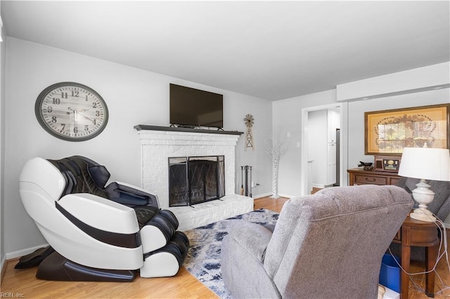 living area featuring baseboards, a brick fireplace, and wood finished floors