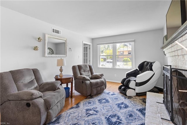 living room featuring baseboards, a fireplace, wood finished floors, and visible vents