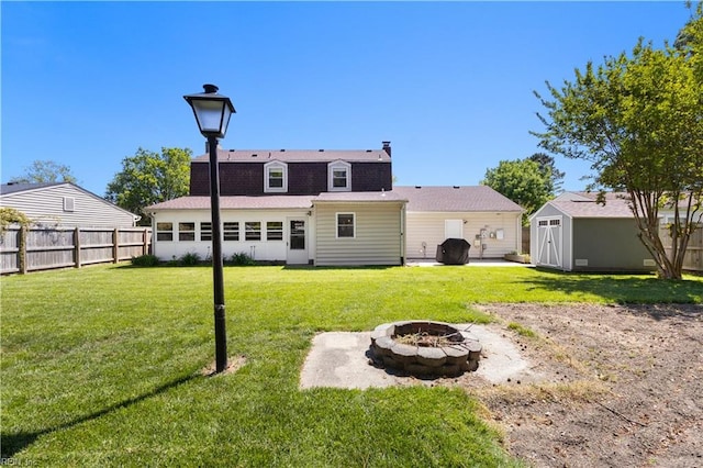 back of property with fence, an outdoor structure, a shed, an outdoor fire pit, and a yard