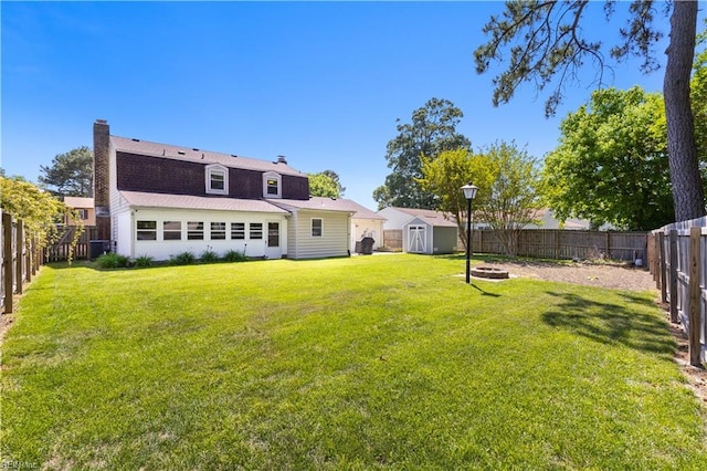 rear view of property featuring a chimney, a storage shed, a lawn, an outdoor structure, and a fenced backyard