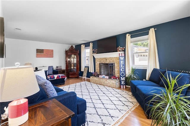 living room with a brick fireplace, visible vents, and wood finished floors