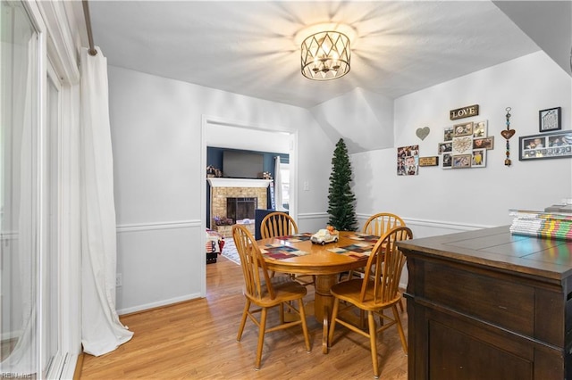 dining room with light wood-style floors, baseboards, and a brick fireplace