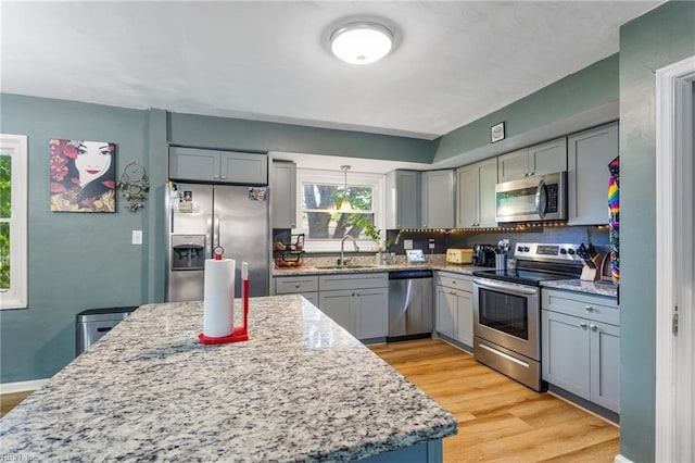 kitchen with light stone countertops, a sink, gray cabinets, stainless steel appliances, and light wood-type flooring