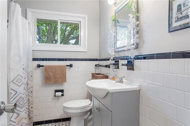 bathroom featuring a shower with curtain, tile walls, a wainscoted wall, vanity, and toilet