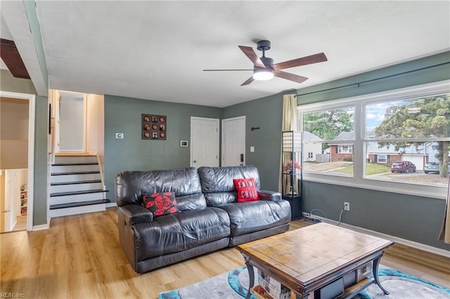 living area with a ceiling fan, stairway, and light wood-style floors