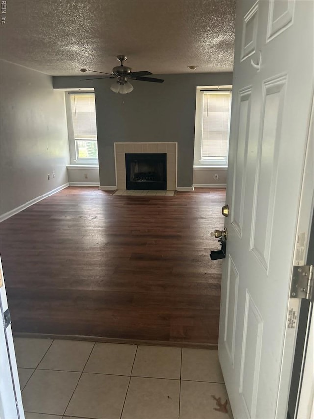 unfurnished living room featuring a fireplace, a textured ceiling, a ceiling fan, baseboards, and wood finished floors