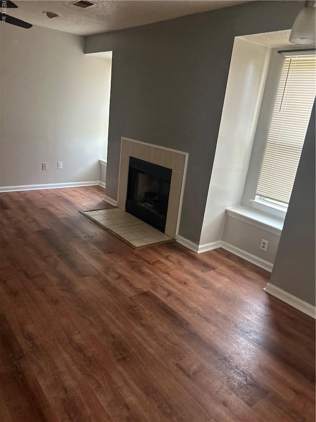 unfurnished living room featuring a tiled fireplace, baseboards, ceiling fan, and wood finished floors