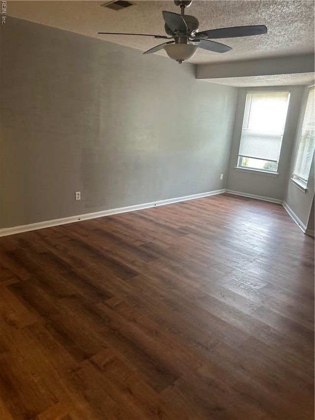 empty room with a textured ceiling, a ceiling fan, baseboards, visible vents, and dark wood-style floors