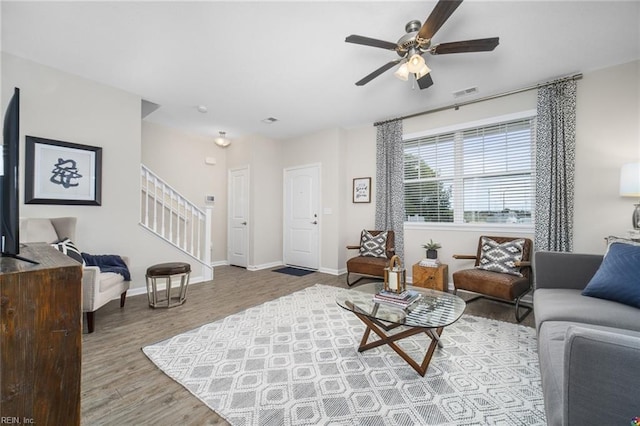 living area featuring baseboards, a ceiling fan, stairs, and wood finished floors