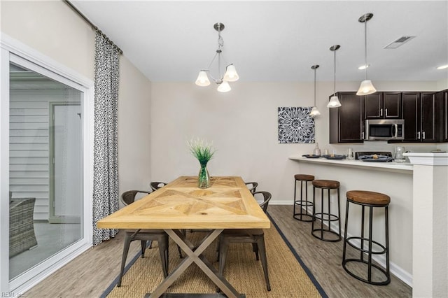 dining area with baseboards, visible vents, an inviting chandelier, and light wood finished floors