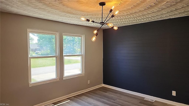 empty room with an inviting chandelier, baseboards, visible vents, and dark wood-type flooring