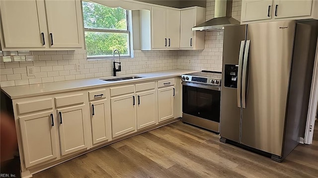 kitchen with a sink, light countertops, wall chimney exhaust hood, stainless steel appliances, and wood finished floors