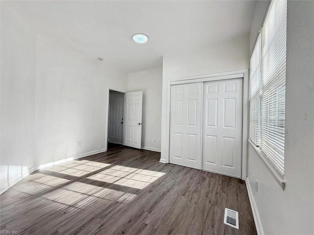 unfurnished bedroom featuring baseboards, visible vents, wood finished floors, and a closet